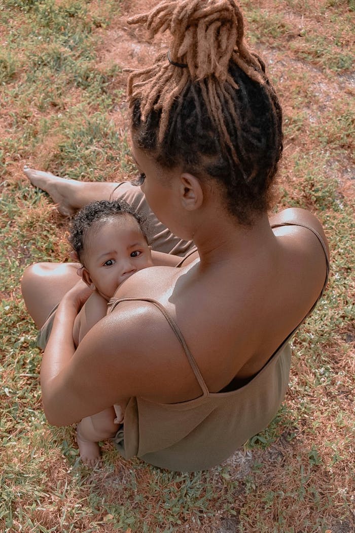 A tender moment of a mother breastfeeding her baby while sitting outside on a sunny day.