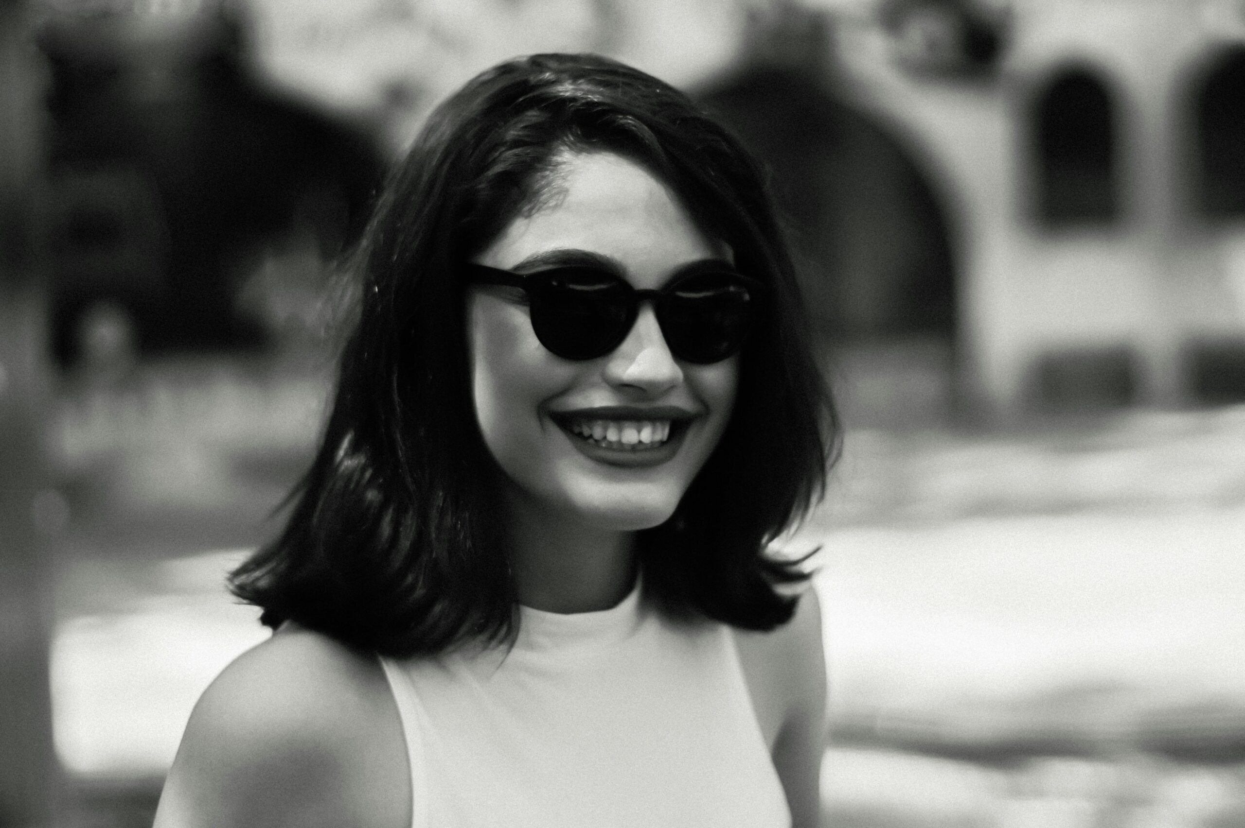 Elegant black and white portrait capturing a smiling woman in sunglasses outdoors in Kutaisi, Georgia.