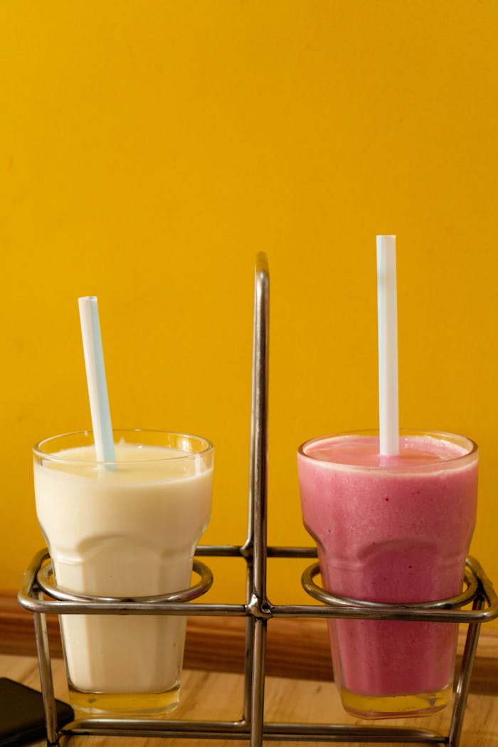 Refreshing fruit shakes in glass cups with straws against a vibrant yellow backdrop.